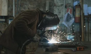 Un profesional de la soldadura realiza tareas de soldadura en un ambiente seguro con el uso completo de equipo de protección personal (EPP).